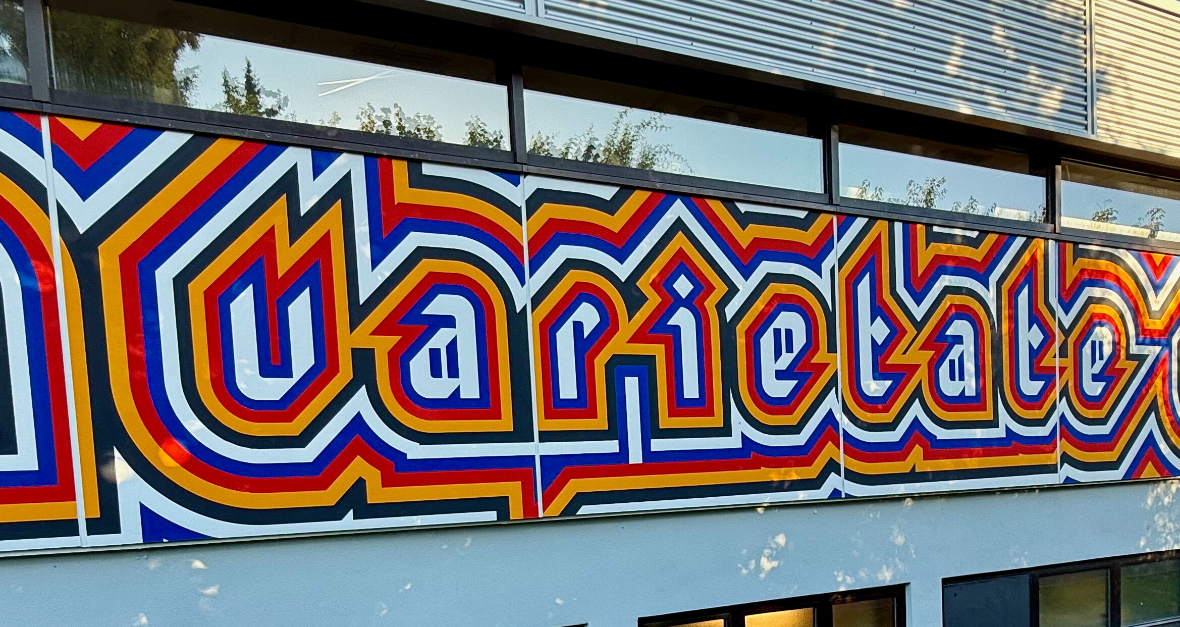 Bunte Graffiti-Buchstaben formen das Wort "Varietate" auf einer modernen Gebäudefassade