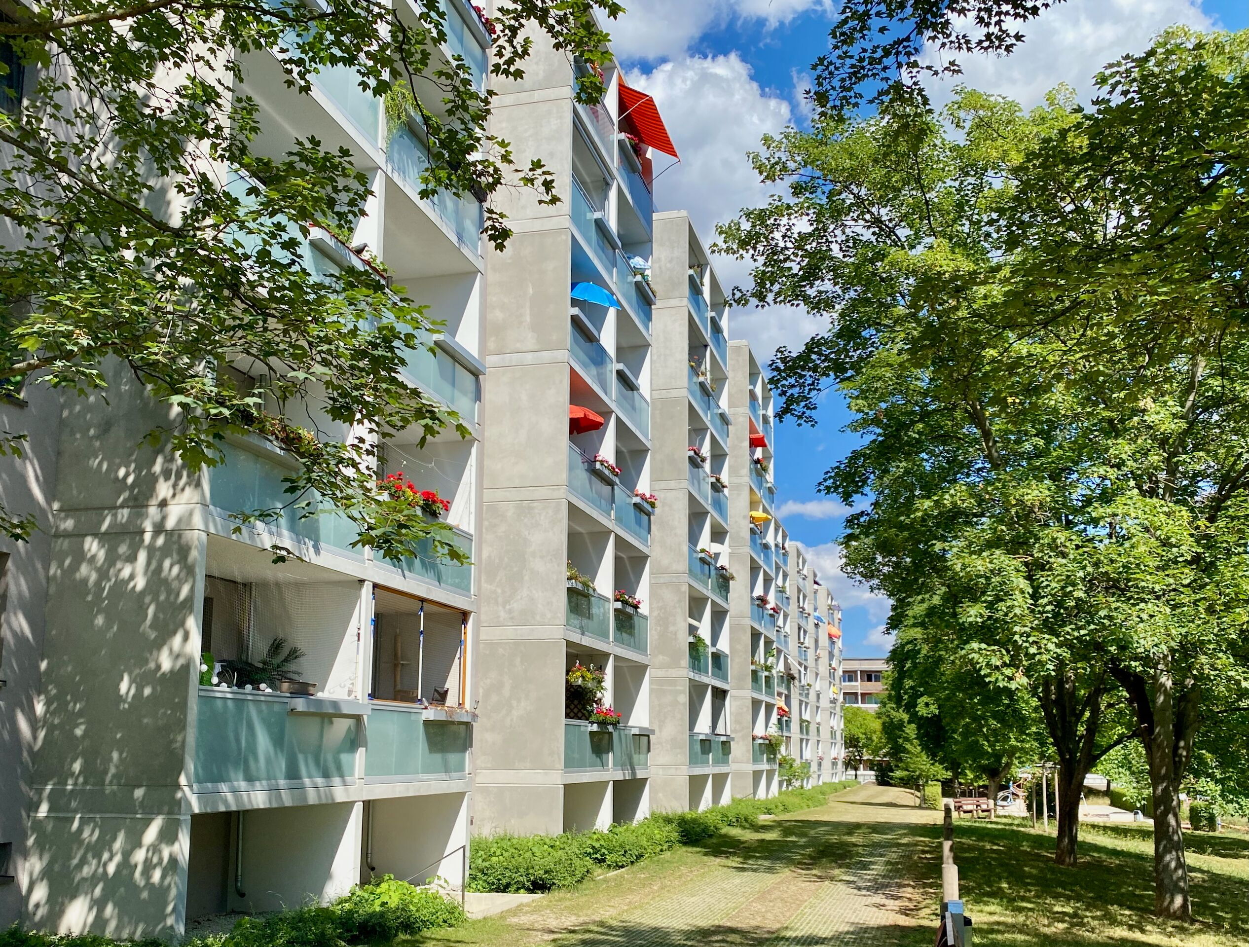 Ein Wohngebäude in Winzerla mit bunten Markisen und Balkonen, eingebettet in grüne Bäume