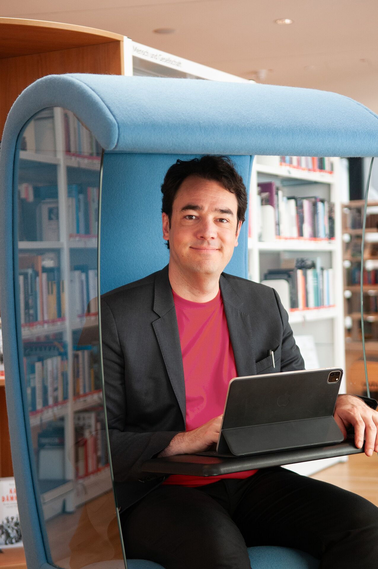 Matthias Warkus sitzt mit einem Laptop in einer gemütlichen Bibliotheksecke und arbeitet an Contenterstellung und Lektorat.