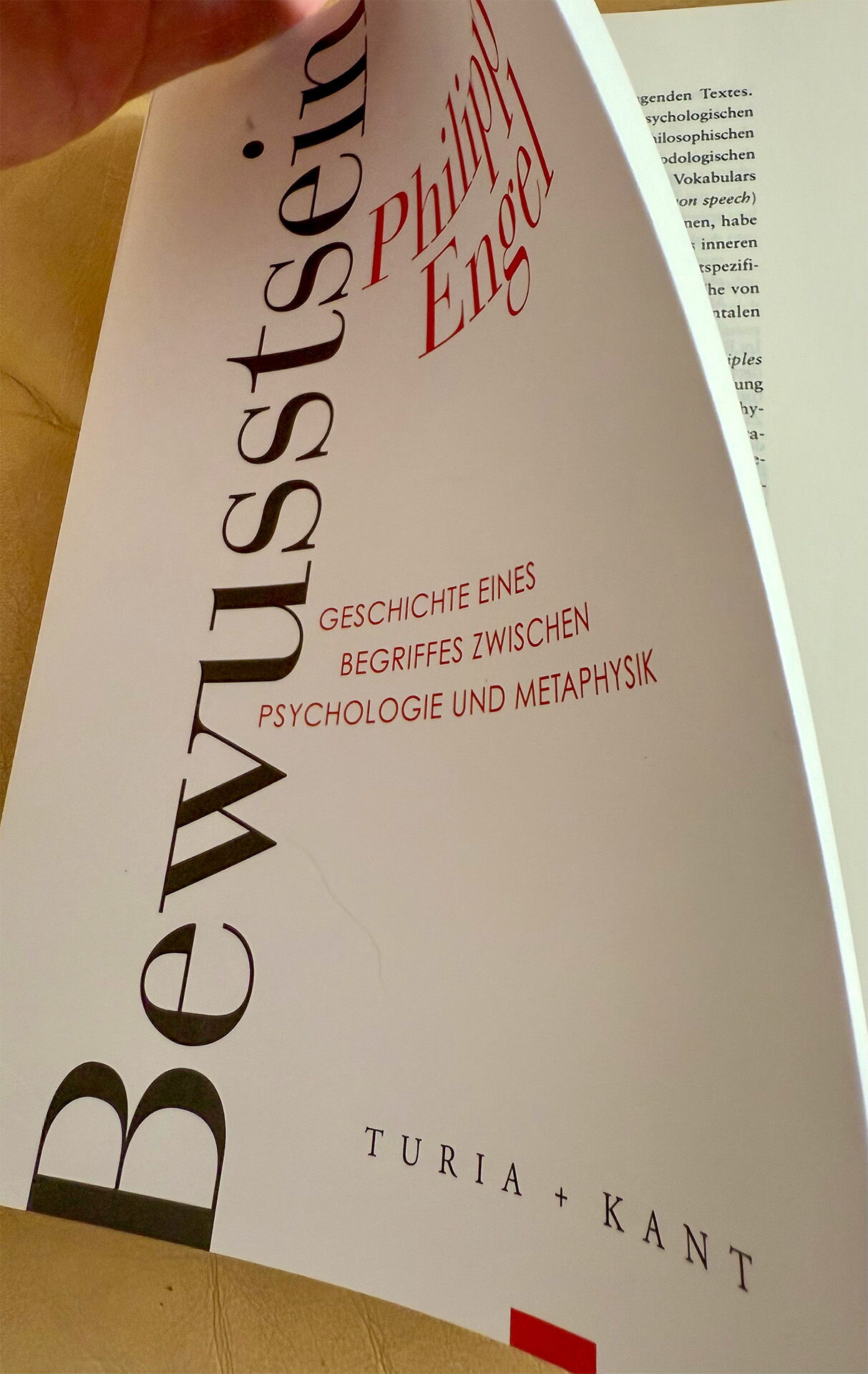 Eine Hand blättert in einem Buch mit dem Titel "Bewusstsein" von Philipp Engel, veröffentlicht von Turia + Kant